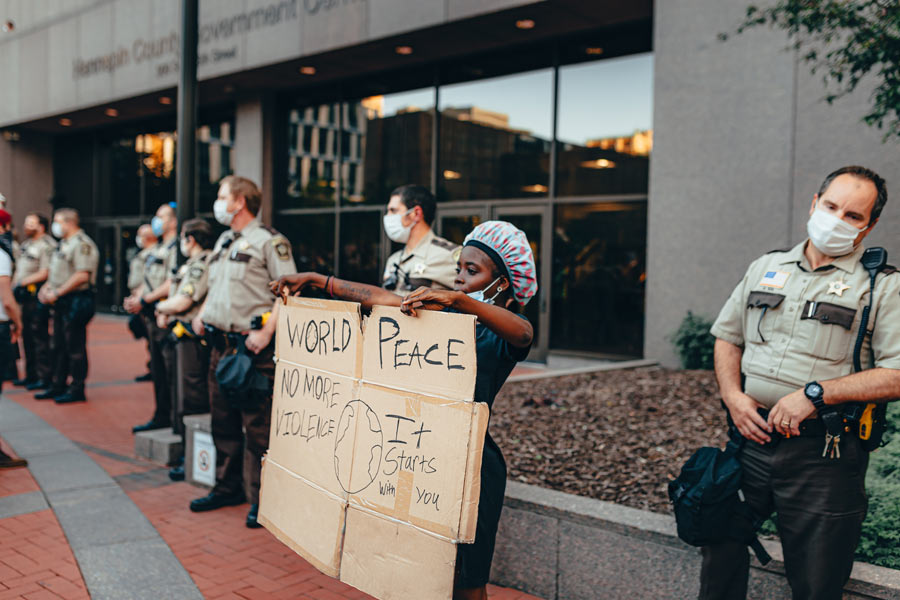 A protestor in Minneapolis holds a sign that says "World Peace. No More Violence. It Starts With You."