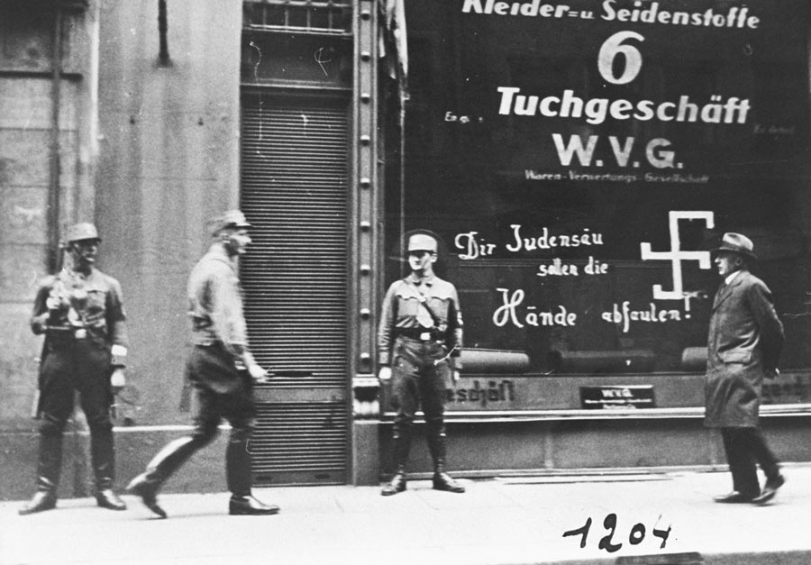 More than 50 years after Baha’u’llah’s passing Nazi storm troopers are seen guarding a Jewish-owned business in Vienna shortly after the Anschluss. The graffito on the store window reads, “You Jewish pig, may your hands rot off!”